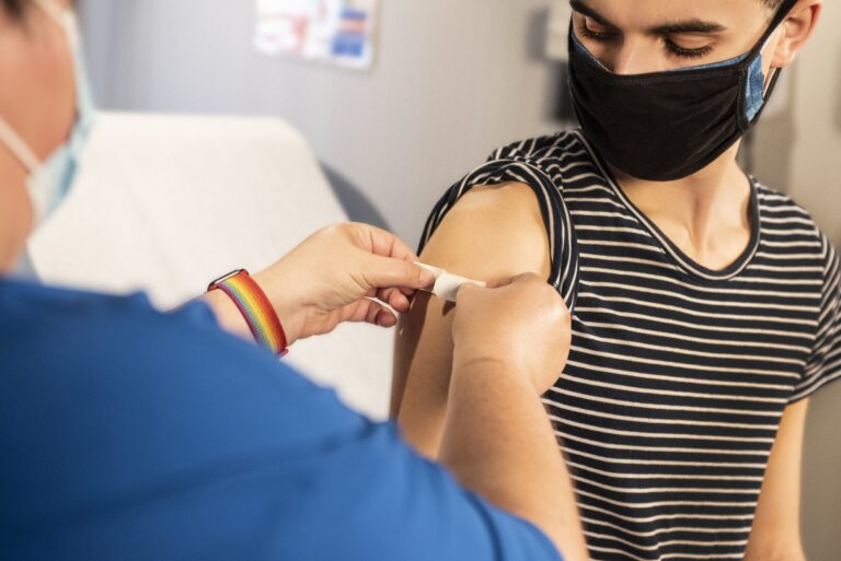 ワクチン接種後に上腕に絆創膏を貼ってもらうマスク姿の若者